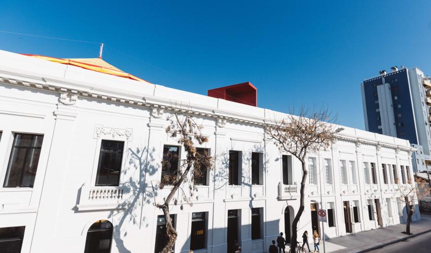 Imagen horizontal de la fachada de NAVE. Es un edificio blanco con ventanas. 